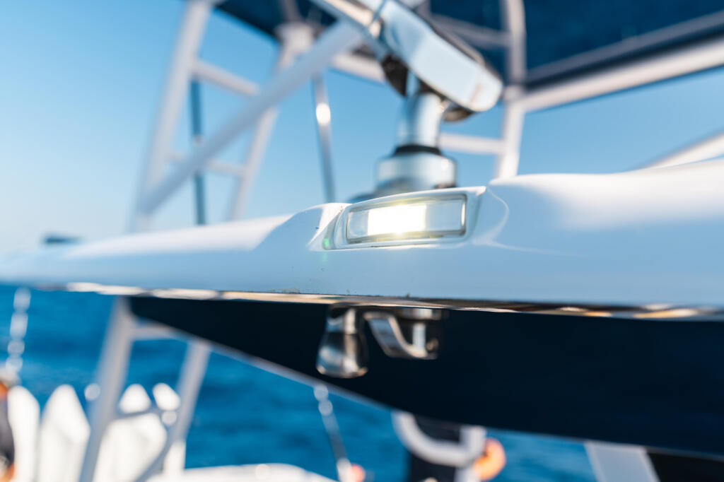 Close-up of white deck lighting fixture mounted on hardtop rail with blue ocean and boat structure in background