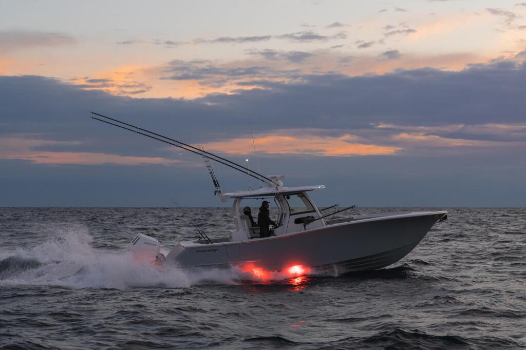 Fishing boat running offshore at dusk with illuminated underwater lights glowing red beneath the hull