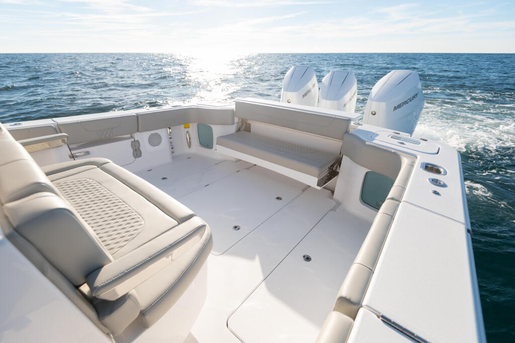 Open cockpit with cream-colored seating, console with electronics, and triple Mercury outboard engines visible on a boat anchored offshore
