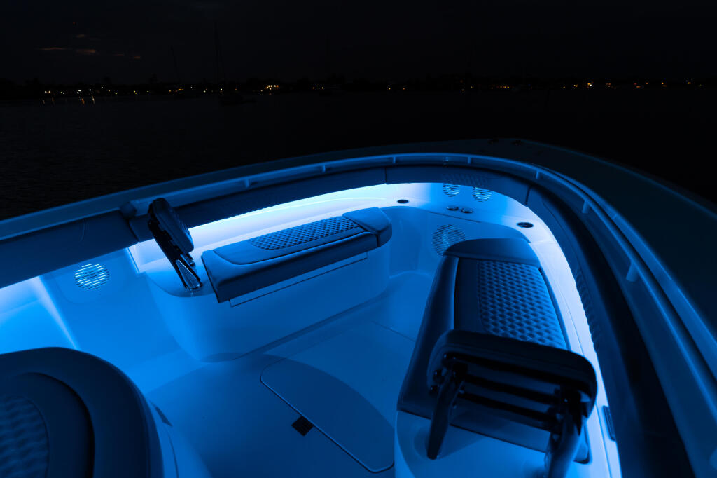 Boat cabin interior illuminated by blue LED lighting at night, showing seating and storage areas
