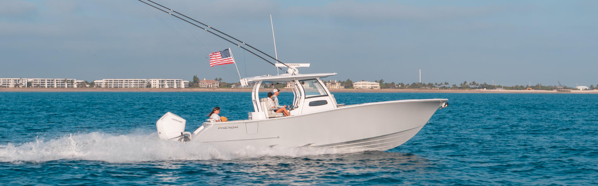 White center console boat running offshore near a sandy beach with a couple aboard and American flag flying
