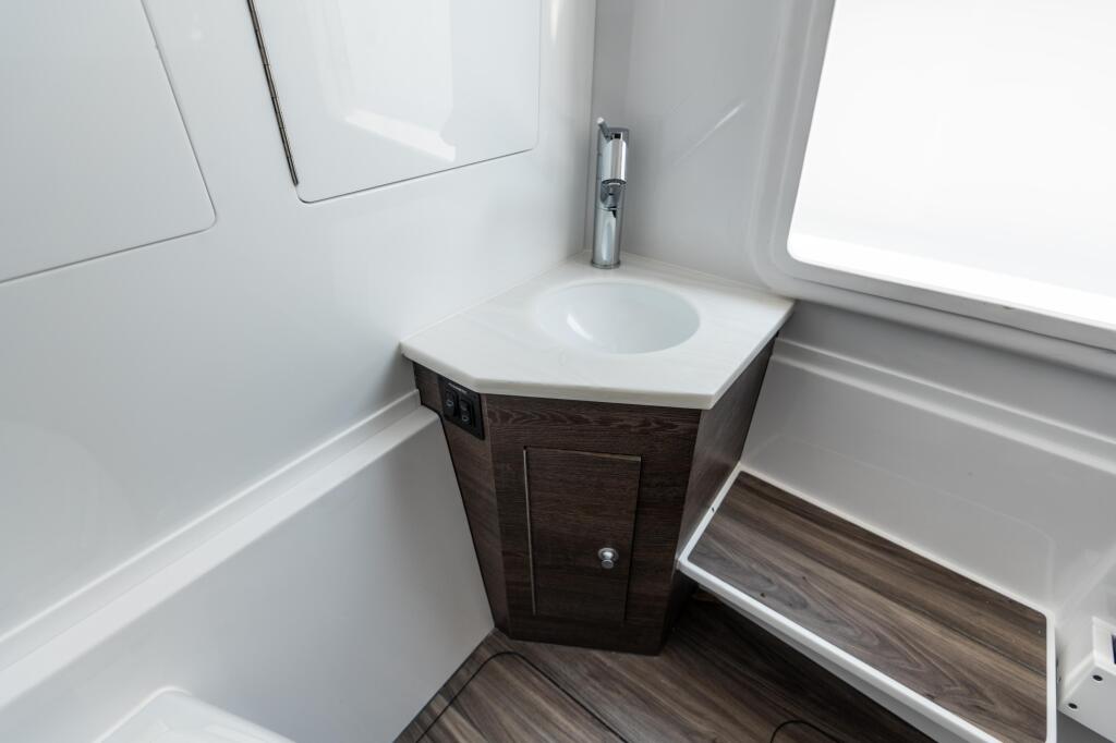 Compact boat cabin bathroom with dark wood vanity, white porcelain sink, and chrome faucet