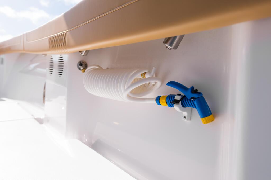 Fresh water spigot and hose coiled on boat cabin wall with blue spray nozzle attached