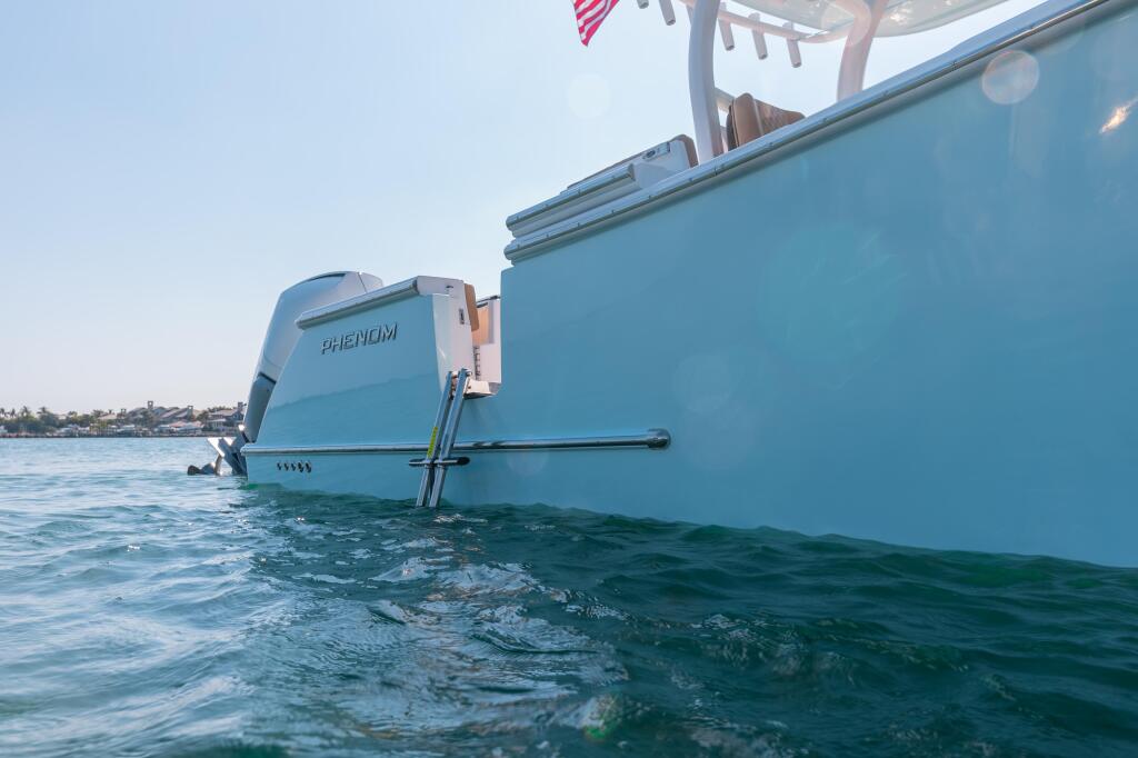 Light blue Phenom boat anchored in shallow coastal water with engine visible at stern