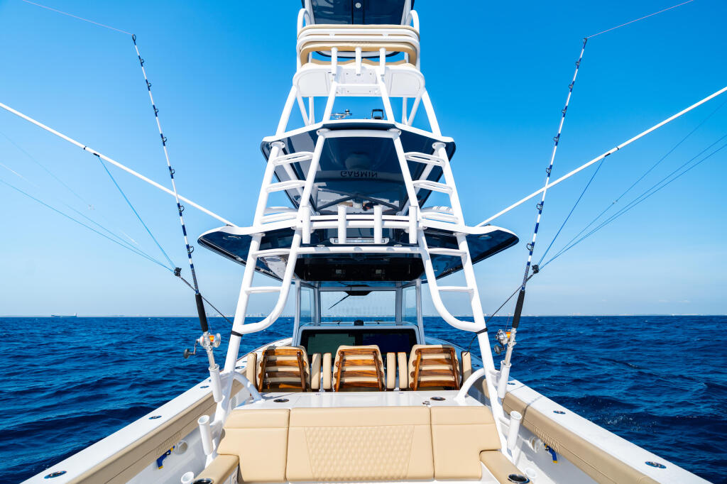 Sport fishing yacht with white hard-top tower, dual outriggers, and fighting chairs under clear blue sky offshore