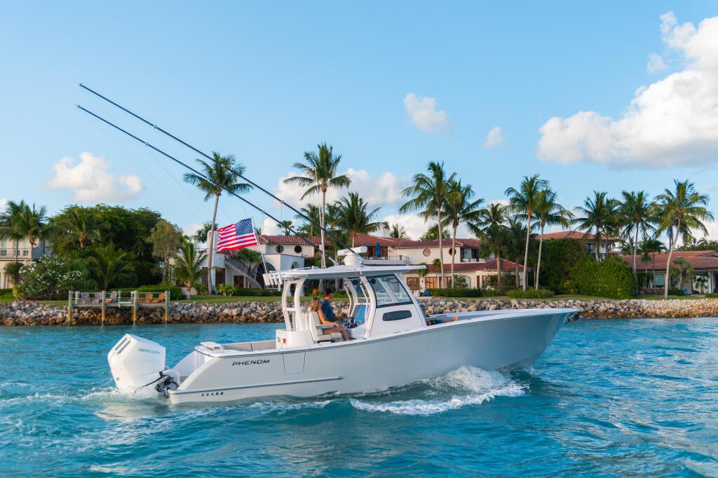 White Phenom boat running offshore with passengers, waterfront homes and palm trees in background