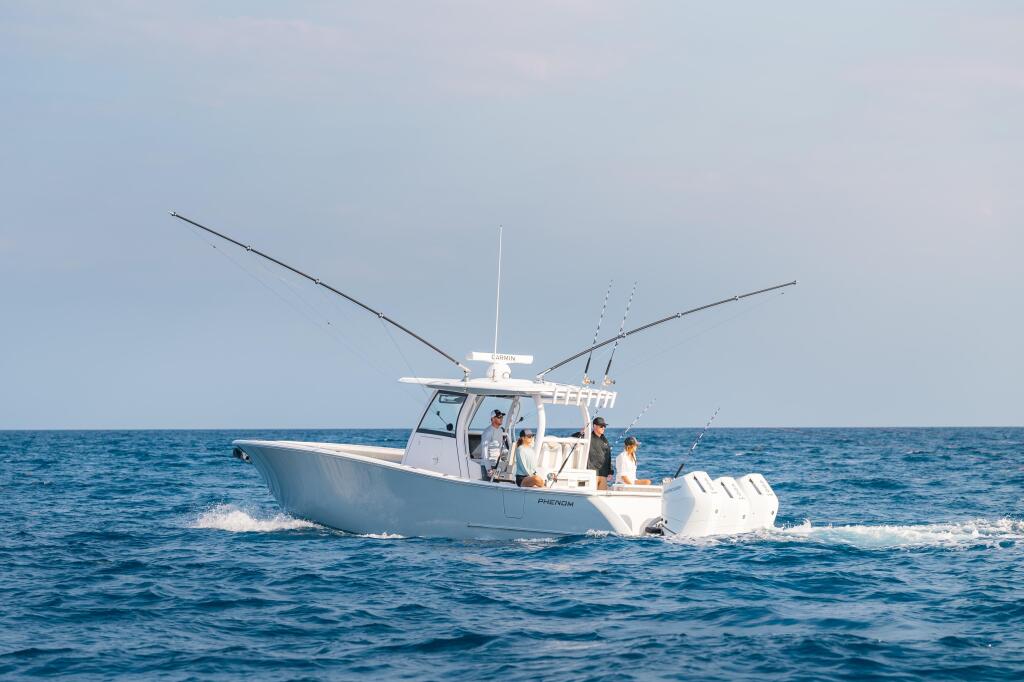 White fishing boat with multiple outrigger poles extended, running through ocean swells with anglers aboard