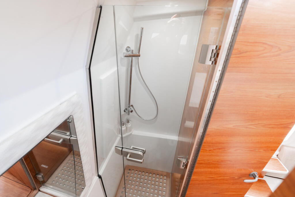 Modern enclosed shower with glass door, rainfall showerhead, and teak flooring in boat cabin