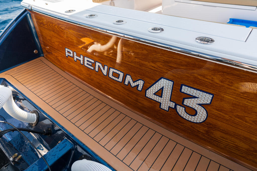 Phenom 45 boat name displayed on rich wooden hull with chrome lettering and teak-style decking