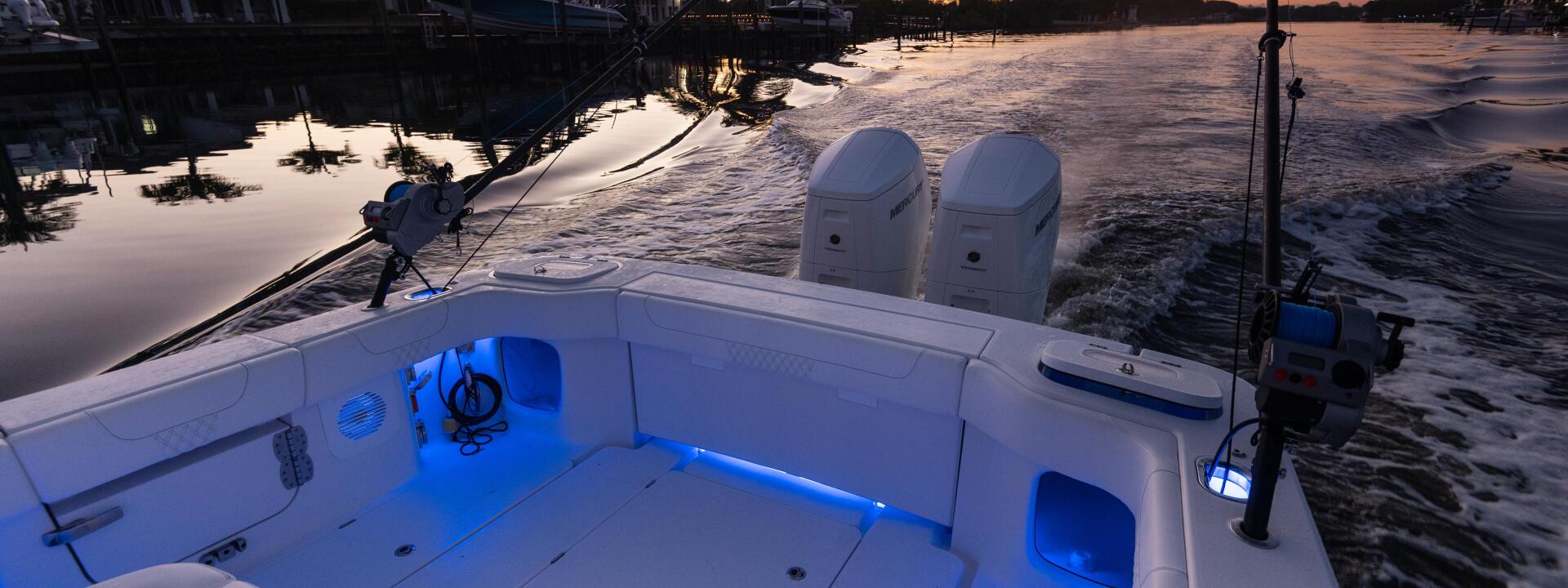 White fishing boat with blue accent lighting docked at a marina at sunset, with waterfront homes and palm trees in background