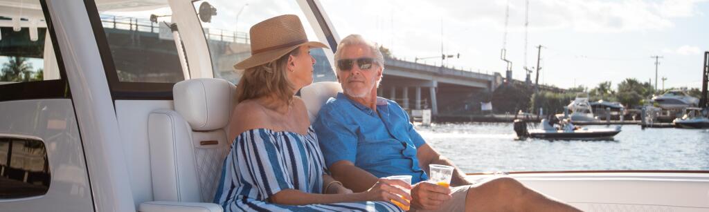 Couple relaxing on the stern seating of a docked boat with marina in background