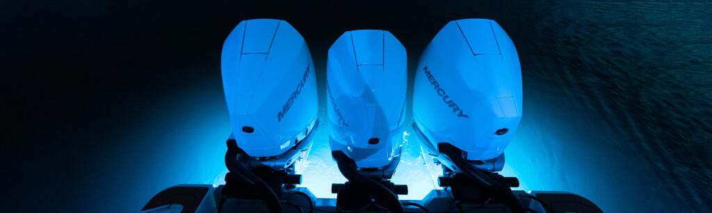 Three illuminated outboard engines glowing blue against dark water at night
