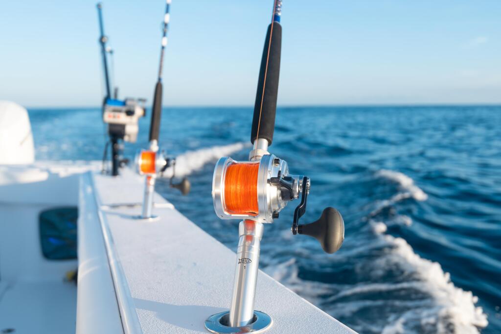 Fishing reels with orange line mounted on boat gunwale overlooking open ocean