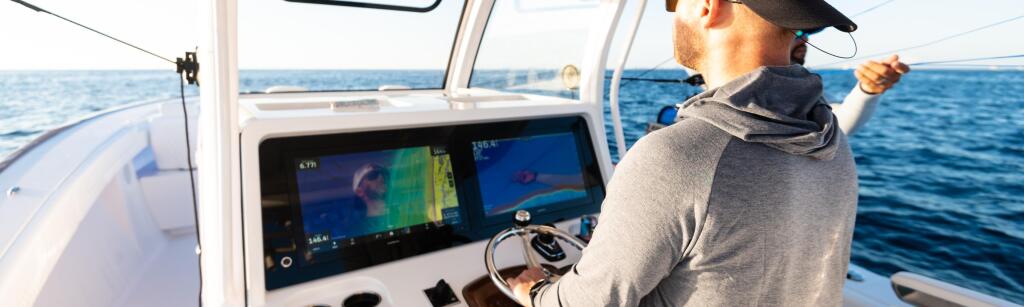 Angler at helm using advanced electronics and sonar display while cruising offshore in calm blue waters