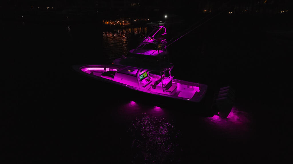 Performance boat illuminated with vibrant magenta LED lighting at night, docked at a marina
