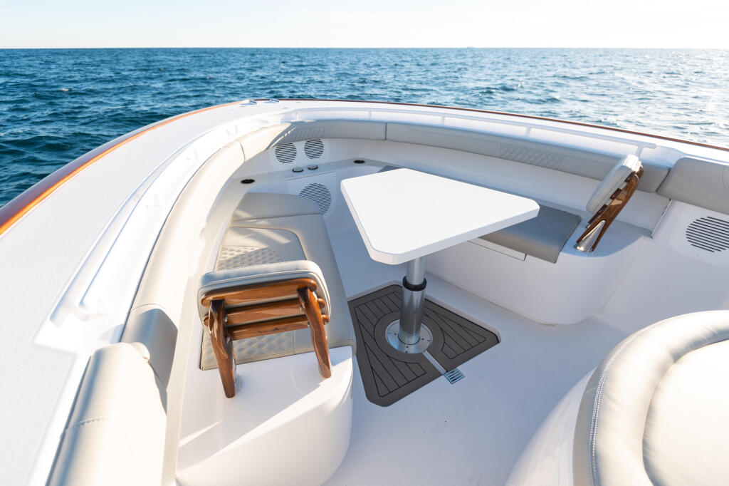 Bow seating area with white cushioned seats, wooden chair, and fiberglass table overlooking open ocean