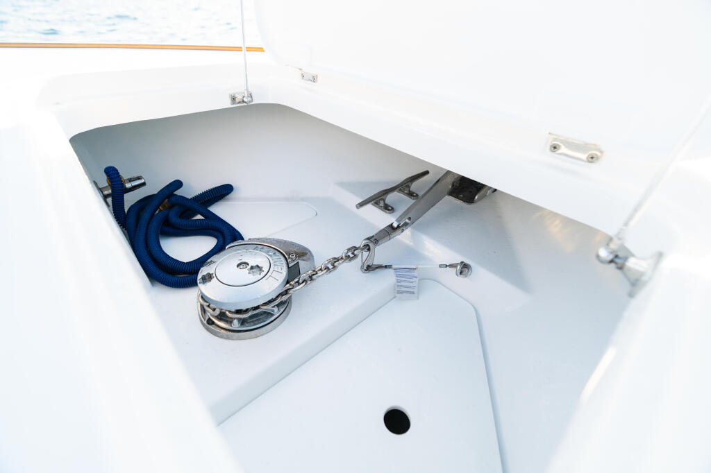 Boat's forward storage locker showing coiled blue rope, stainless steel anchor, and mechanical hardware