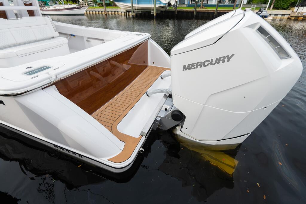 White boat with Mercury engine docked at marina showing wood-trimmed cockpit and bustling waterfront in background