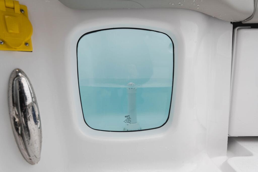 Cabin windshield with tinted glass framed by white interior wall, steering wheel visible to the left