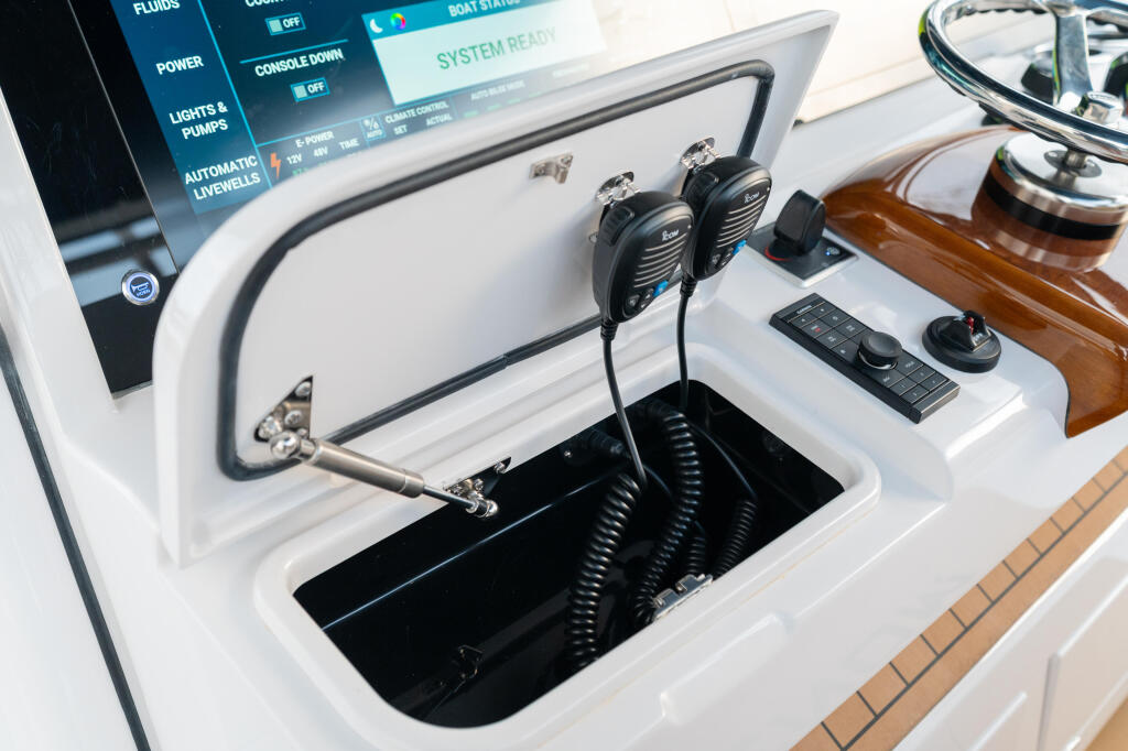 Helm console showing VHF radio microphones, control panel with power and livewell switches, and electronic keypad mounted above storage compartment