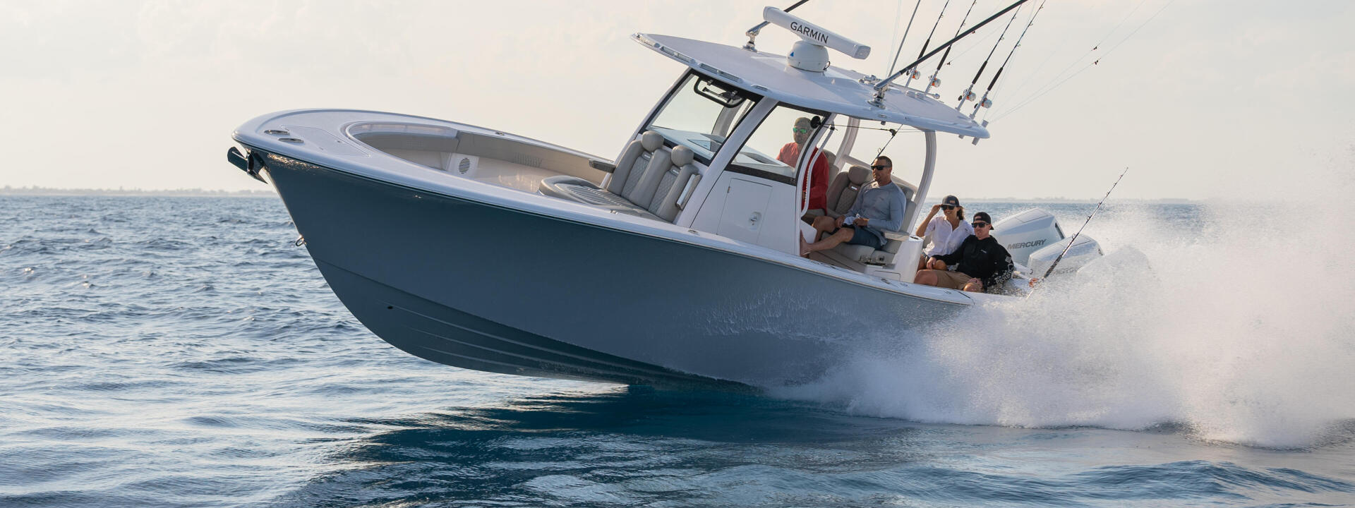 Family cruising in a blue and white center console boat approaching the beach with fishing rods mounted on the hard-top