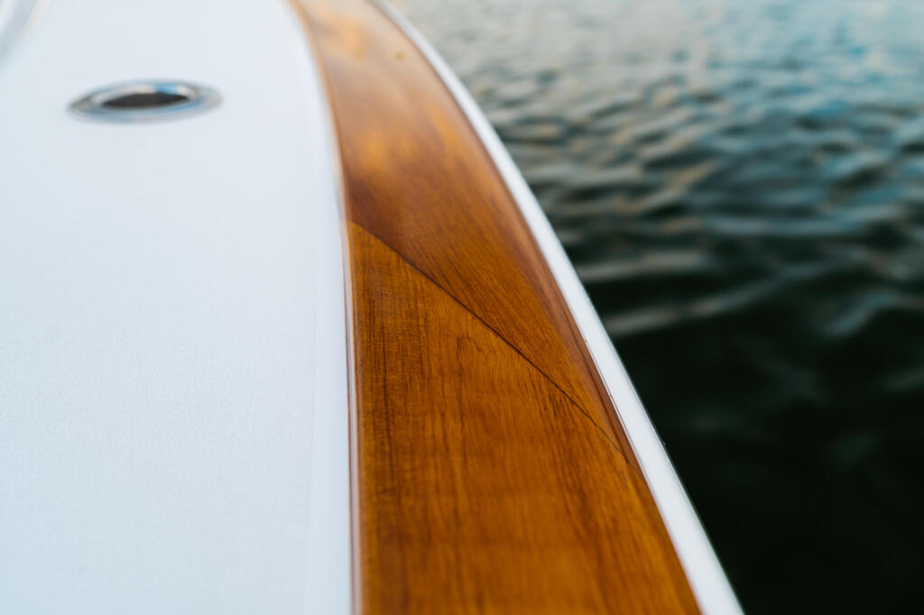 Close-up of a boat's white gunwale with faux-teak toe rail detail beside rippling water