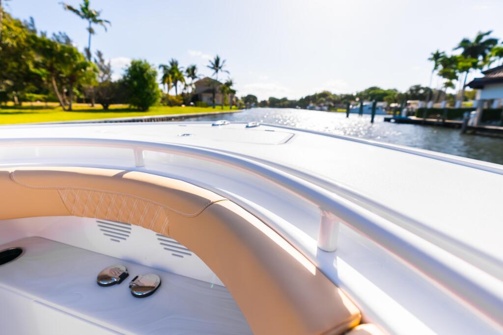 Boat bow with tan leather seating and white hardtop cruising past waterfront homes with palm trees
