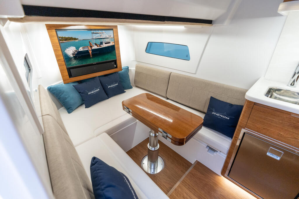 Boat cabin interior with cream seating, wood-grain accents, a teak table, flat-screen TV, and blue cabin cushions