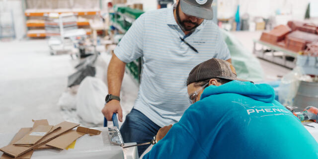 Two technicians working on boat electronics installation at a manufacturing facility