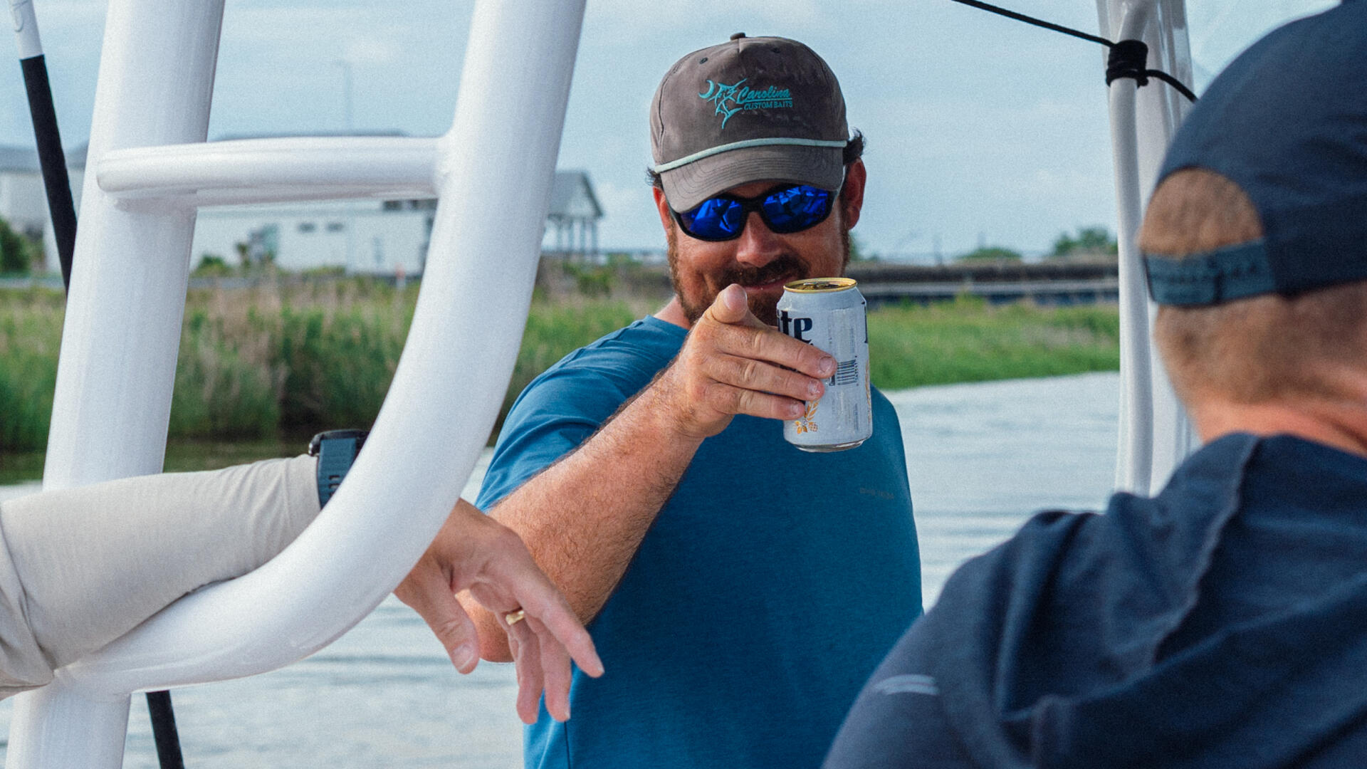 Man in blue shirt and sunglasses holding a drink aboard a center console fishing boat with hard-top and white railings