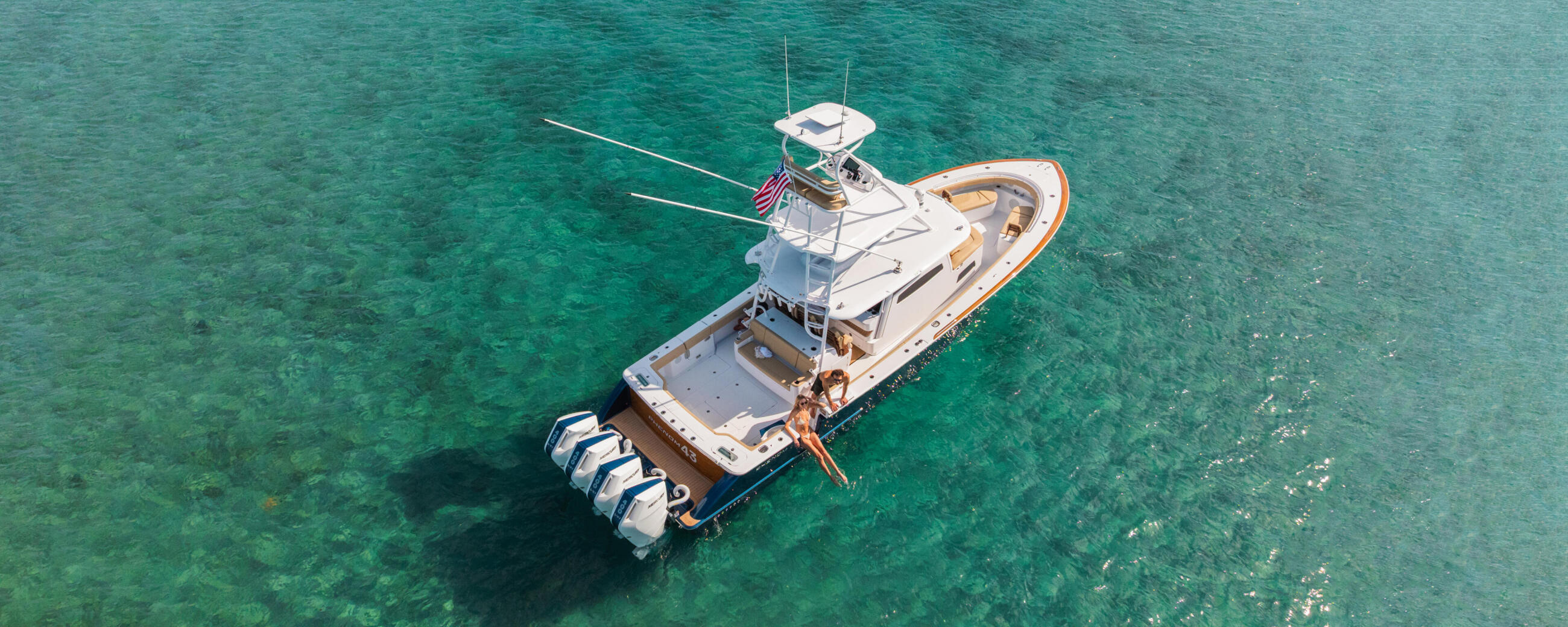 Aerial view of a white and tan center console fishing boat anchored in crystal clear turquoise water