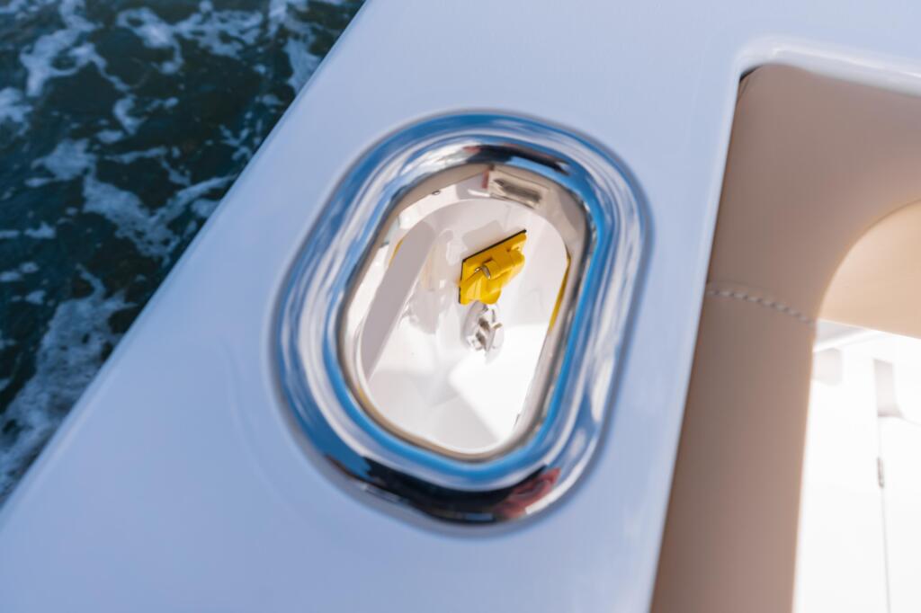 Polished chrome hawse pipe with yellow rope fitting on white boat hull above water