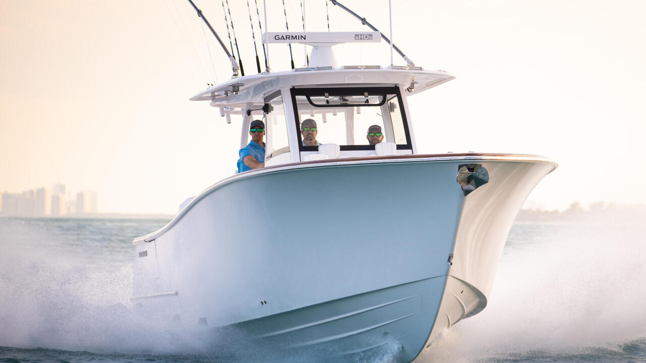 Blue and white fishing boat running through offshore waves with anglers aboard and fishing rods mounted on hard-top