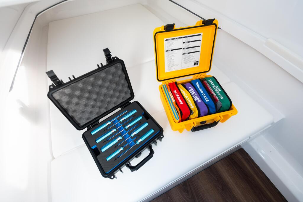 Two organized storage cases on a white cabin shelf: black case with blue tools and yellow case with colorful safety equipment and documentation