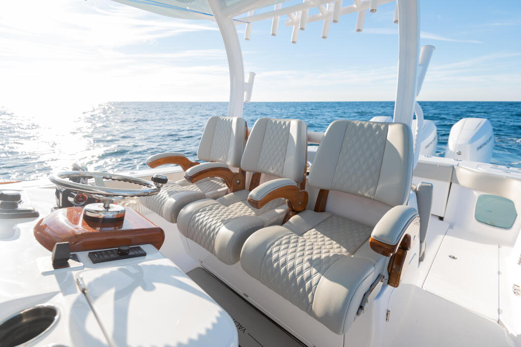 Triple white quilted captain's chairs with teak armrests and hardtop shade on open boat cockpit overlooking blue ocean