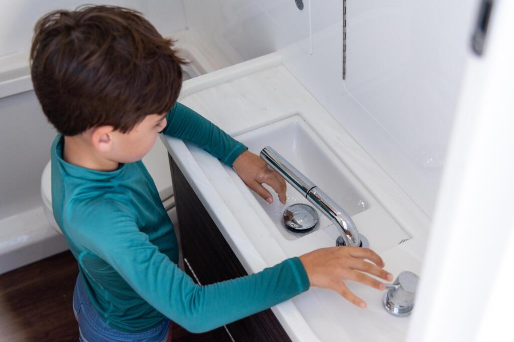 Child using faucet at galley sink in boat cabin with pull-out spray head
