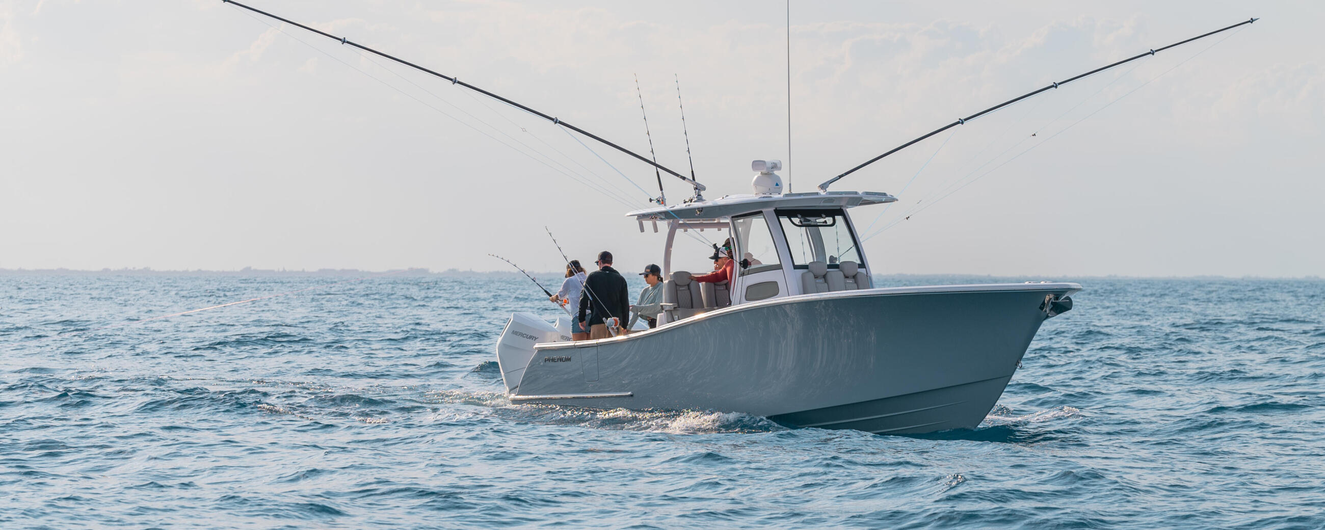 Fishing boat with anglers and fishing rods deployed, running offshore in calm blue waters