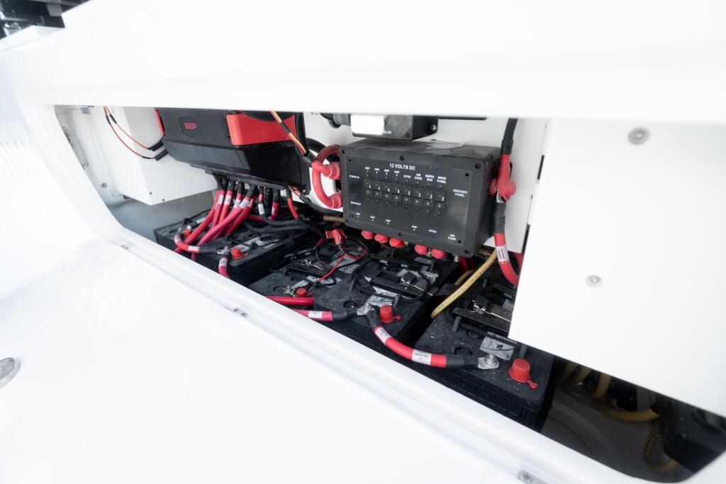 Boat's electrical system with 100-amp battery charger, red cables, and marine electronics mounted in white cabin storage compartment