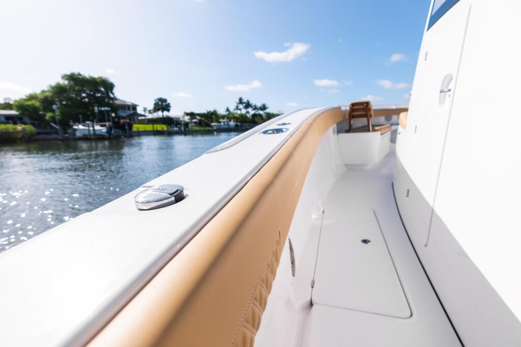 Starboard side deck view of boat with tan bolster cushions and white cabin, moored at marina