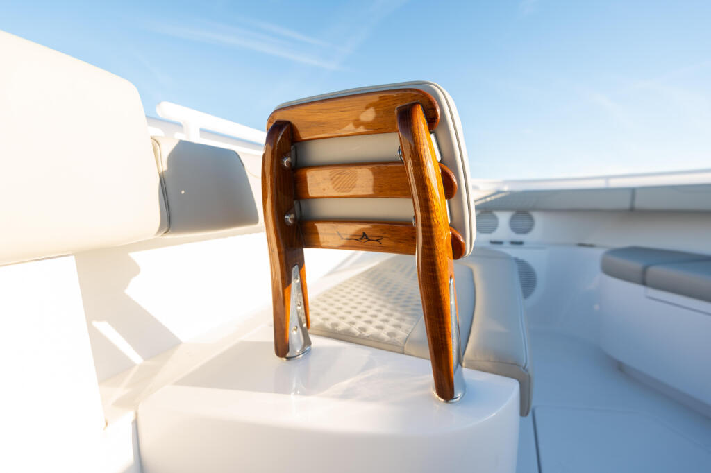 Teak and chrome bow backrest with cushioned seating on a white fiberglass boat deck under clear sky