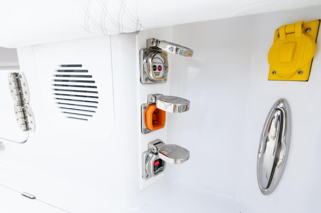 Boat cabin wall displaying electrical outlets, breaker switches, speaker grille, and steering wheel hardware
