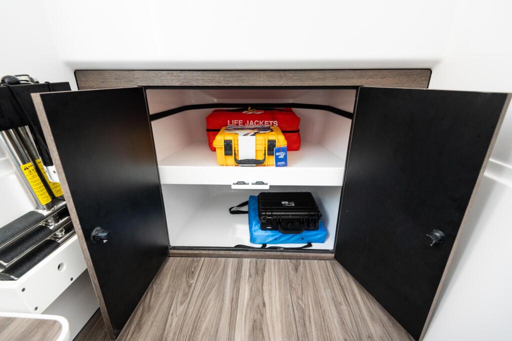 Open cabin storage cabinet displaying red life jackets, yellow emergency kit, and black electronic equipment on white shelves