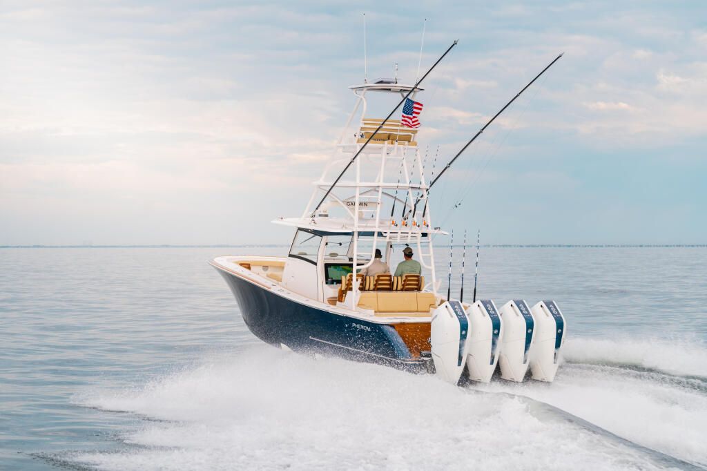 Sport fishing boat with quad engines running through shallow beach waves under clear sky