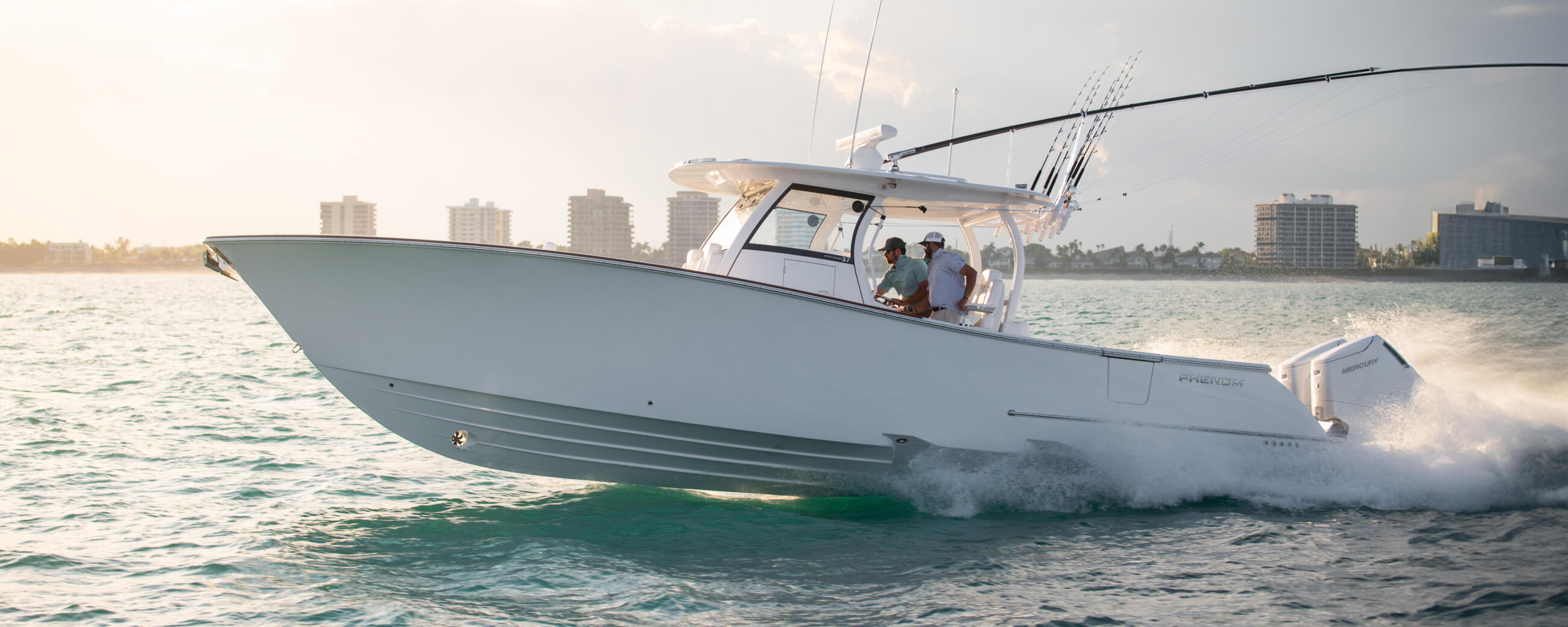 White center console boat running through waves with passengers and fishing rods in coastal waters near high-rise buildings