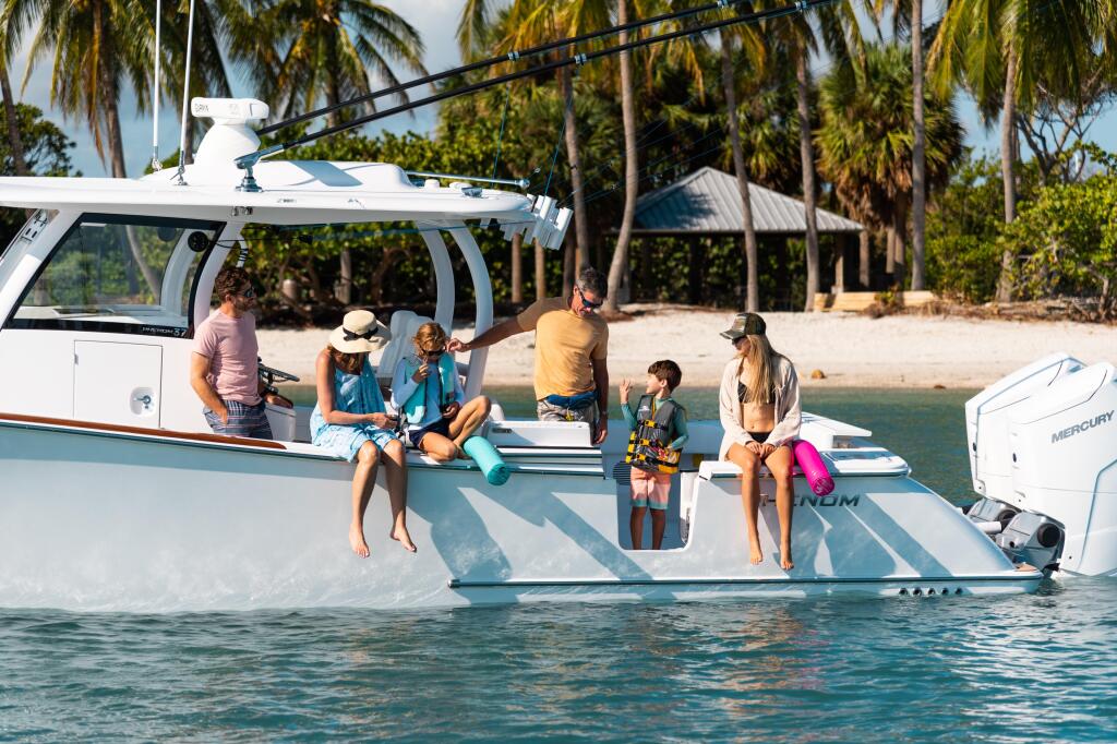 Family and friends enjoying shallow water activities on a center console boat docked at a tropical sandbar with palm trees