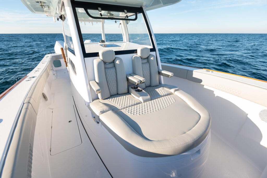 Center console boat with gray cushioned seating, hard-top canopy, and calm blue ocean waters beyond