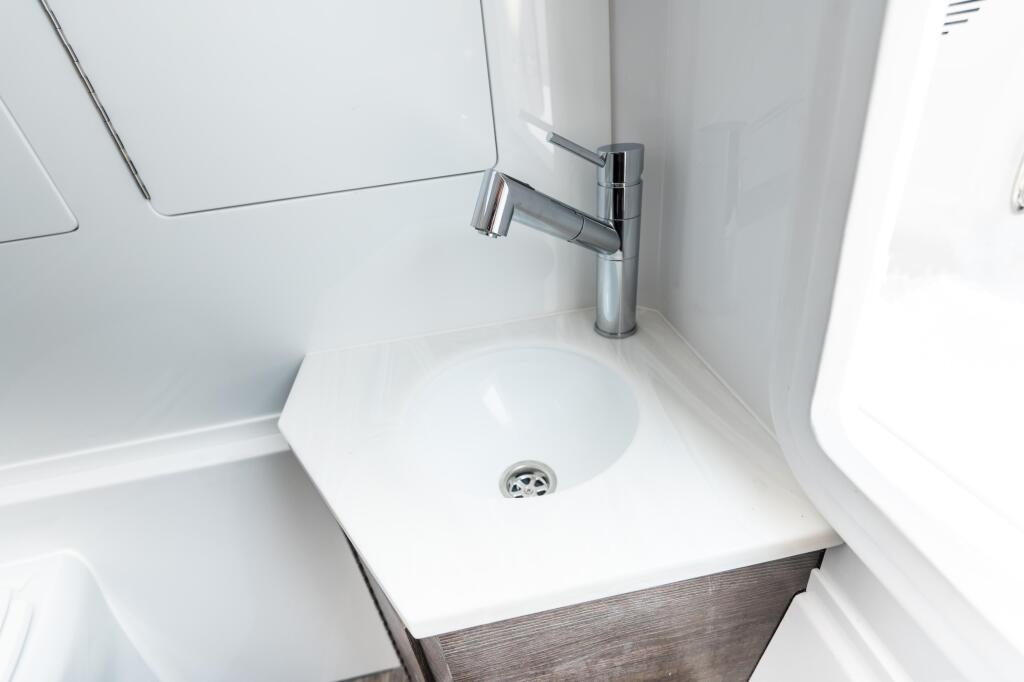Modern white bathroom sink with chrome faucet and wood-grain cabinet in boat cabin
