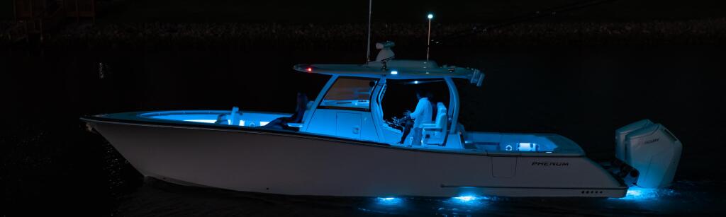 Center console fishing boat illuminated with blue LED lighting at night, docked in calm water near downtown buildings