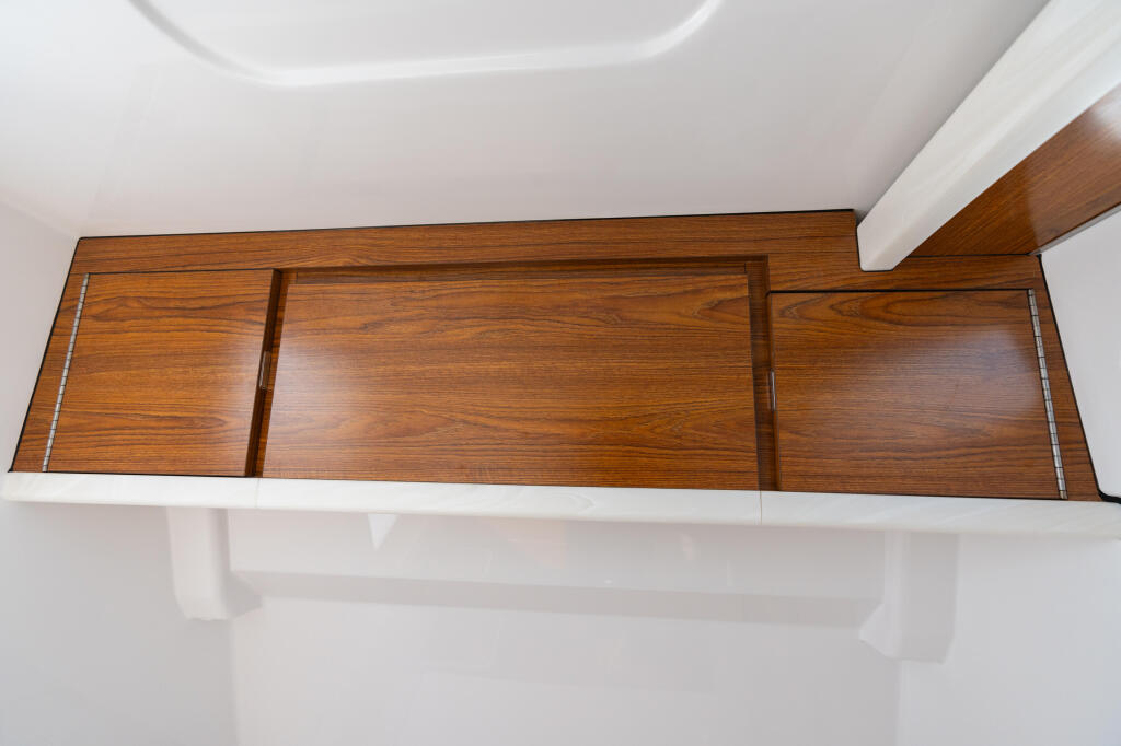 Overhead view of a boat cabin's wooden storage cabinet with multiple compartments and chrome hardware