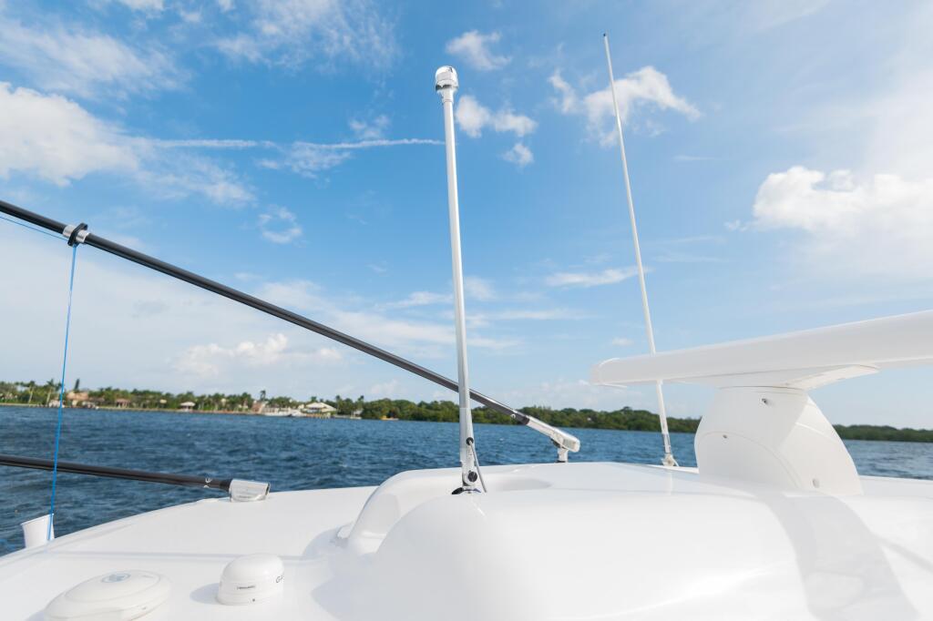 White boat deck with antenna and rigging on calm blue water with shoreline in background